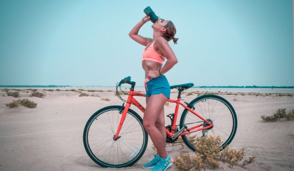 image showing a women cycling in shorts and drinking water